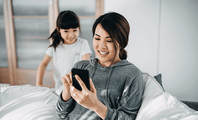 Busy mum checks her smartphone with her little girl looking over her shoulder