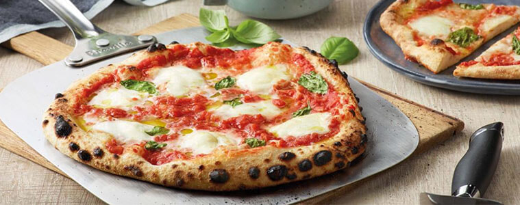 Breville Neapolitan Pizza fresh from the oven on a board with a pizza cutter and basil leaves