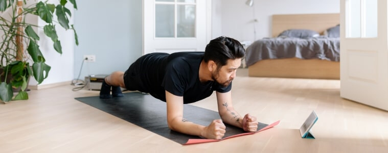 A man works out in his living room at home while watching a fitness video on his tablet