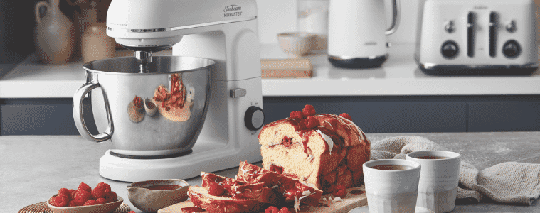 Image of Sunbeam Planetary Mixmaster The Master One sitting on a kitchen bench next to a sliced raspberry cake and two cups of tea