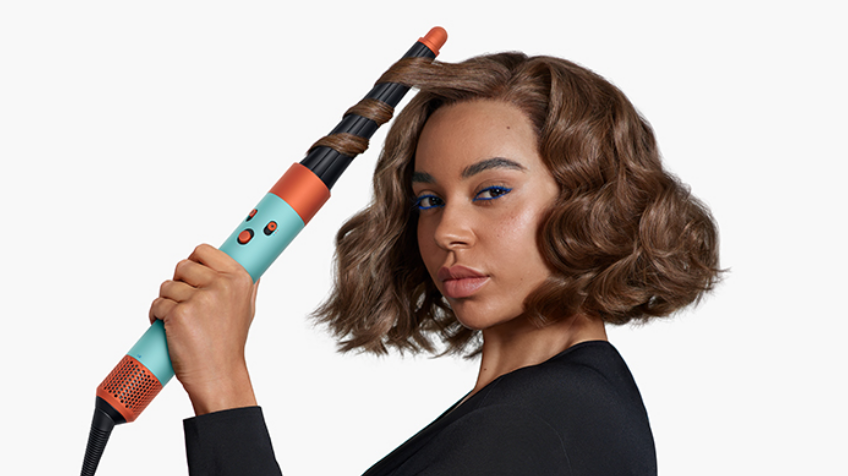 Woman using Dyson Airwrap in silver and gold to curl her hair