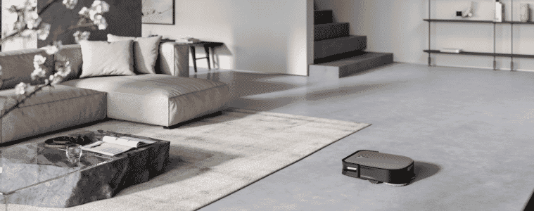 Square robot vaccuum in action on concrete floor 