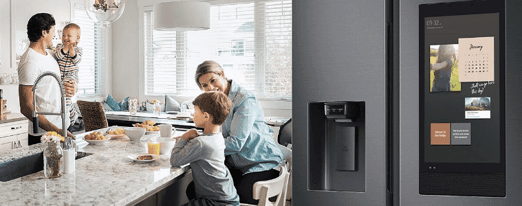A Samsung Family Hub fridge sits off to the side of the kitchen of a young family having breakfast