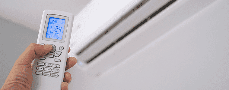 A man holds the remote control of his air conditioner up to the vent adjusting the temperature to 24