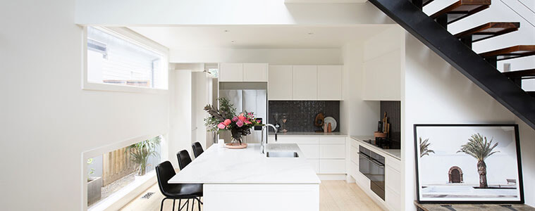 Sideview of lightflooded white kitchen with black stools and black staircase