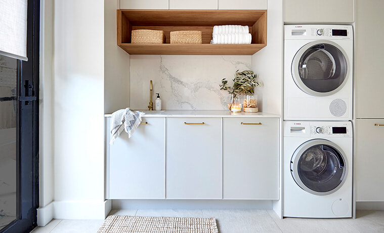 Modern laundry with white cabinetry marble splashback open timber shelf and stacked washing machine and dryer 