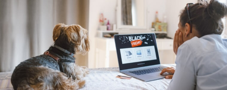 Woman doing her Black Friday research with her dog whilst laying on a bed