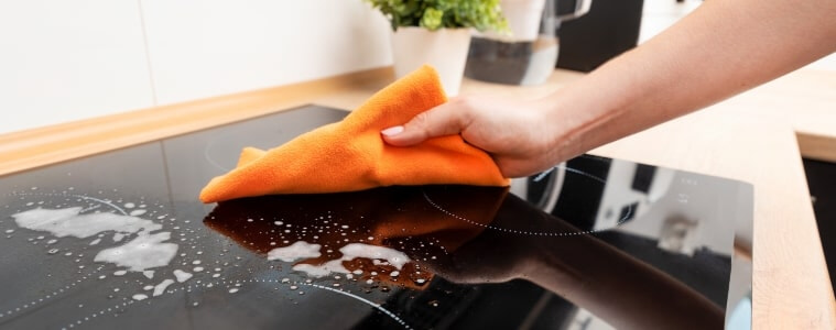A woman uses a cloth to wipe clean her induction cooktop