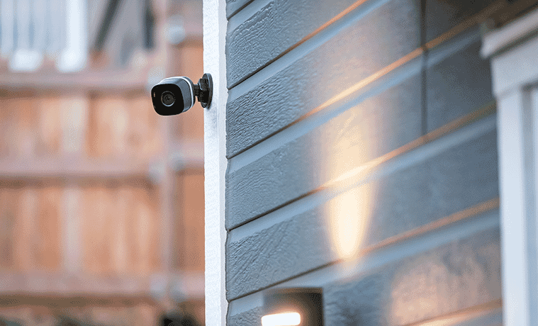 A discreet black surveillance camera mounted high on an exterior wall of a house