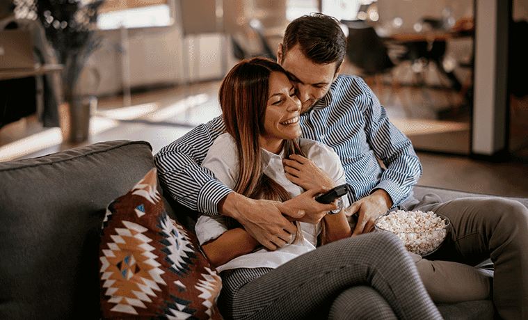 Couple at home cuddling on the couch watching TV