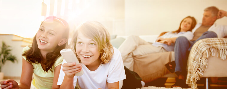 Two kids change the TV channel while their parents watch from the couch