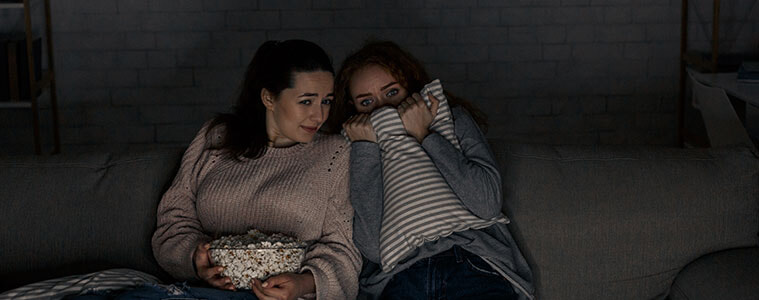Teenage girls watch a scary movie on TV in their living room