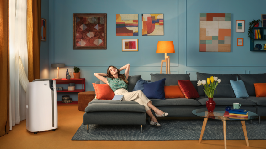 A woman cools down in her living room with a DeLonghi portable air conditioner
