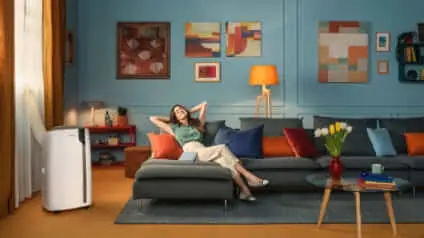 A woman cools down in her living room with a DeLonghi portable air conditioner