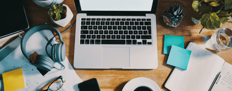 Still life shot of various items on a home office workstation including headphones and a laptop