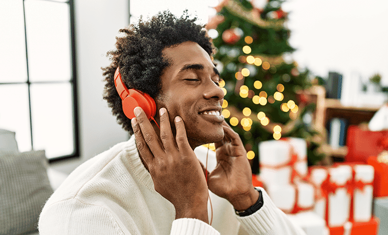 A young man wears headphones to listen to Christmas music while sitting near a Christmas tree