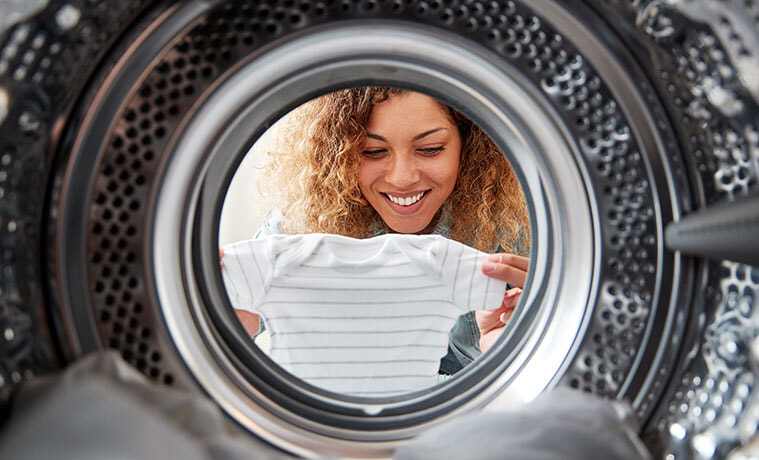 View of woman holding babys clothes and she leans into the open door of a tumble dryer