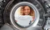 View of woman holding babys clothes and she leans into the open door of a tumble dryer