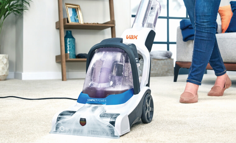 A woman cleans her living room carpet with the Vax Compact Power Carpet Cleaner