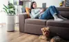 Young woman on a couch adjusts the setting of her home air purifier from her smart tablet