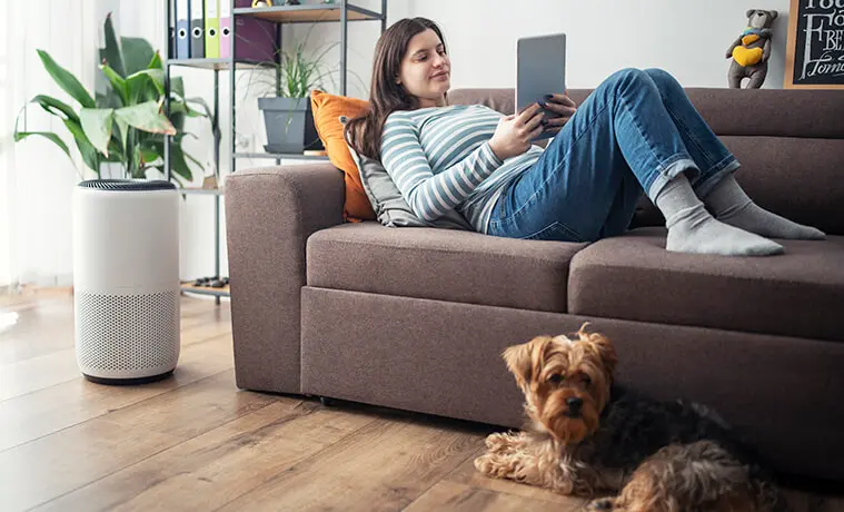 Young woman on a couch adjusts the setting of her home air purifier from her smart tablet