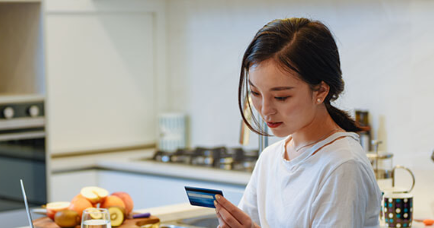 Young woman sitting at kitchen bench with laptop doing her finances
