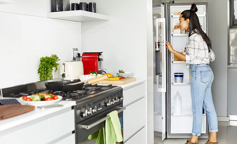 Woman searches for ingredients in her stainless steel fridge while cooking dinner