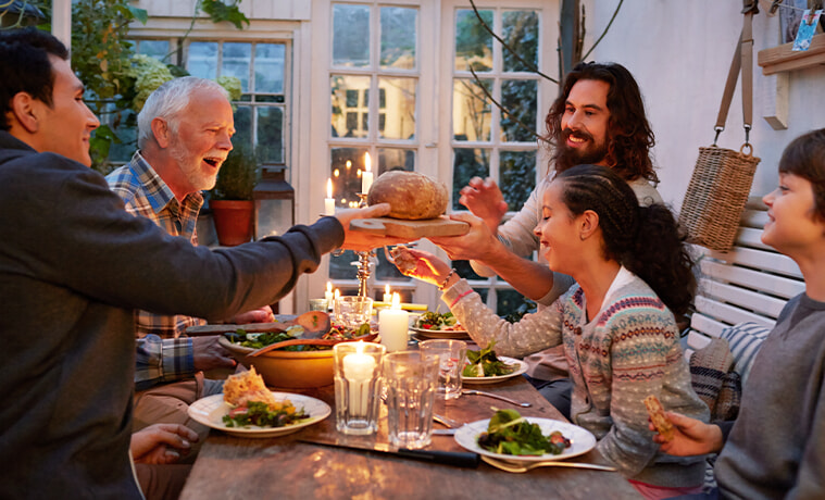 A big family having dinner together around a cosy table and passing a basket of bread to each other