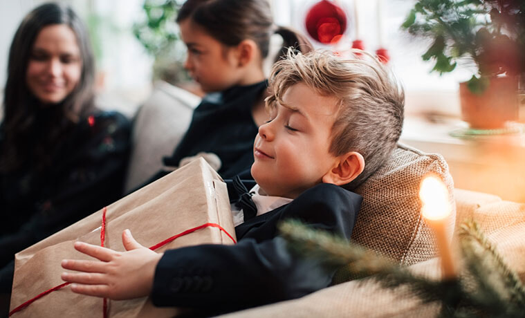 Smiling boy holding a Christmas present while sitting with family