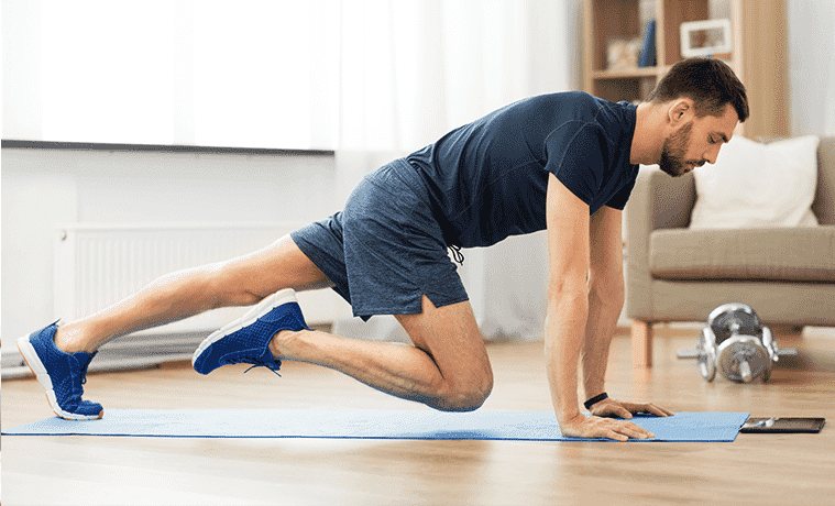 A man works out on a yoga mat at home while wearing a fitness tracker