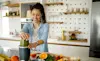 A woman blitzes a green smoothie while standing at her kitchen bench 
