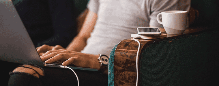 Closeup view of a man using his laptop while waiting for his phone to charge on a charging pad thats plugged into his laptop