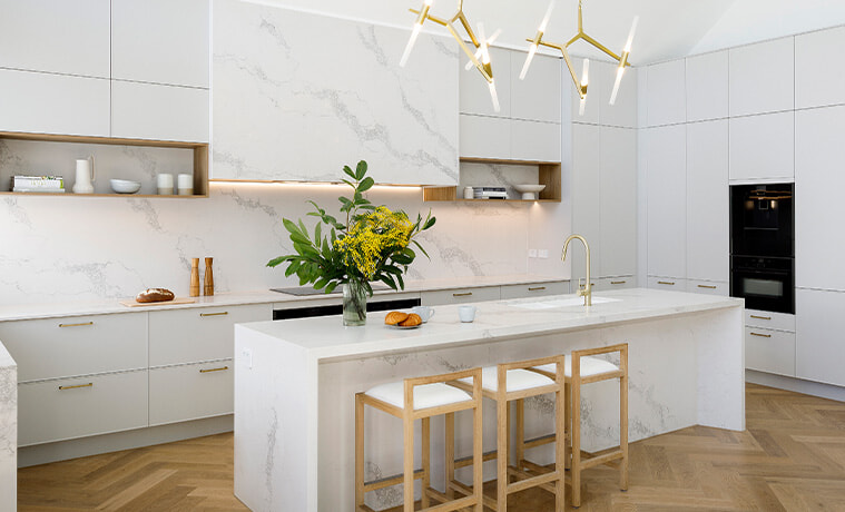 White coastalstyle kitchen with marblelook island and herringbone floors
