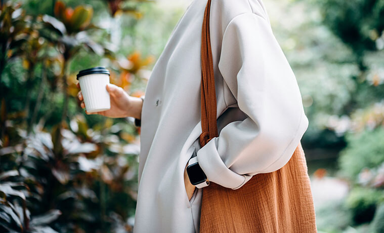 The midsection of a welldressed woman in a cream winter jacket and wearing a smartwatch with a white band and black face