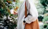 The midsection of a welldressed woman in a cream winter jacket and wearing a smartwatch with a white band and black face
