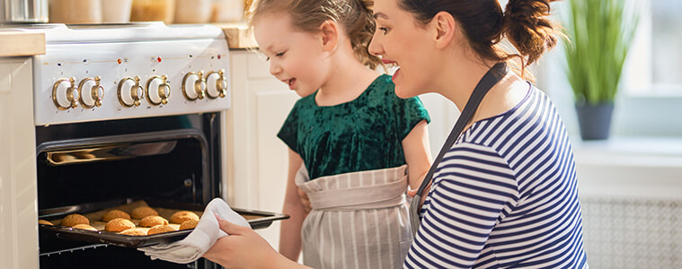 Mother and daughter remove a tray of cookies from a retro style oven with gold control knobs 