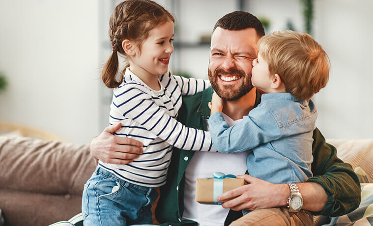 Children sitting with their dad on the couch as they give him a present