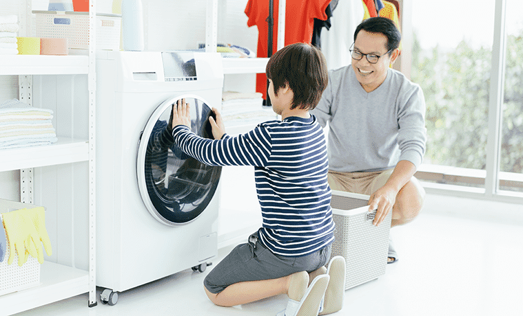 A father shows his son how to use the front loader washing machine in their laundry at home