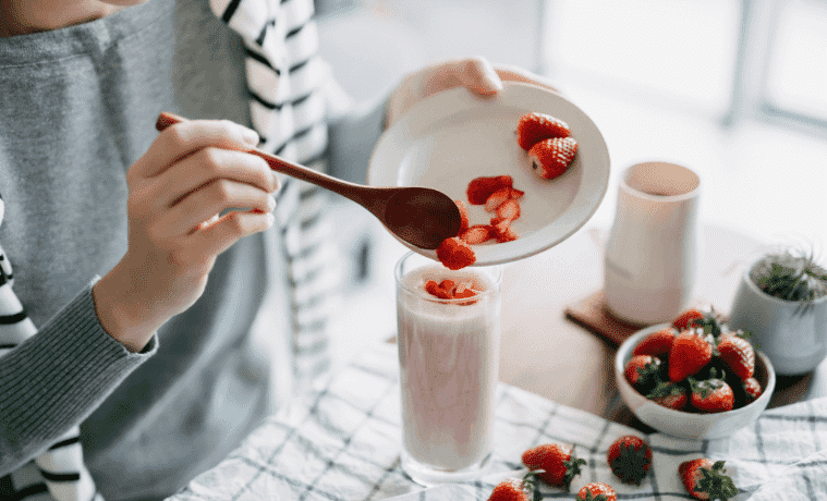 A young woman makes a fresh and healthy strawberry smoothie for breakfast using a blender on her kitchen bench