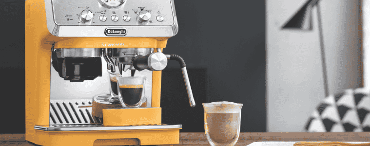 A DeLonghi LaSpecialista Arte Coffee Machine Yellow sits on a kitchen bench a freshly brewed coffee in a glass sits beside it