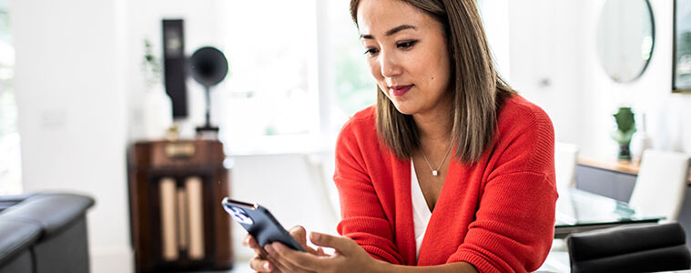 Woman browses on her smartphone while sitting at the breakfast bar in her kitchen