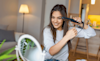 a woman sitting in her living room straightening her hair whilst looking in a mirror 