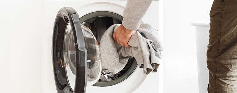 Side view of a man putting clothes in a washing machine in a home laundry