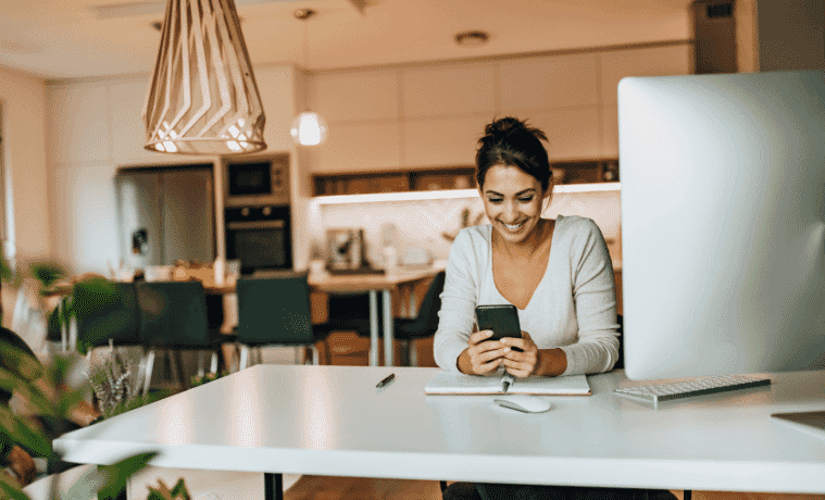 Happy woman using her smart phone whilst working from home