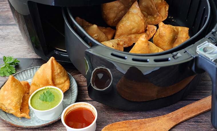 Closeup view of crunchy golden samosas in an air fryer with a plate of samosas in the foreground  