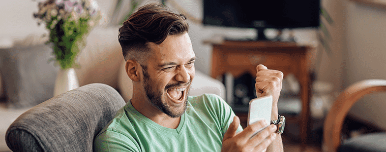 Excited man gets the sports scores on his smartphone while sitting on an armchair at home