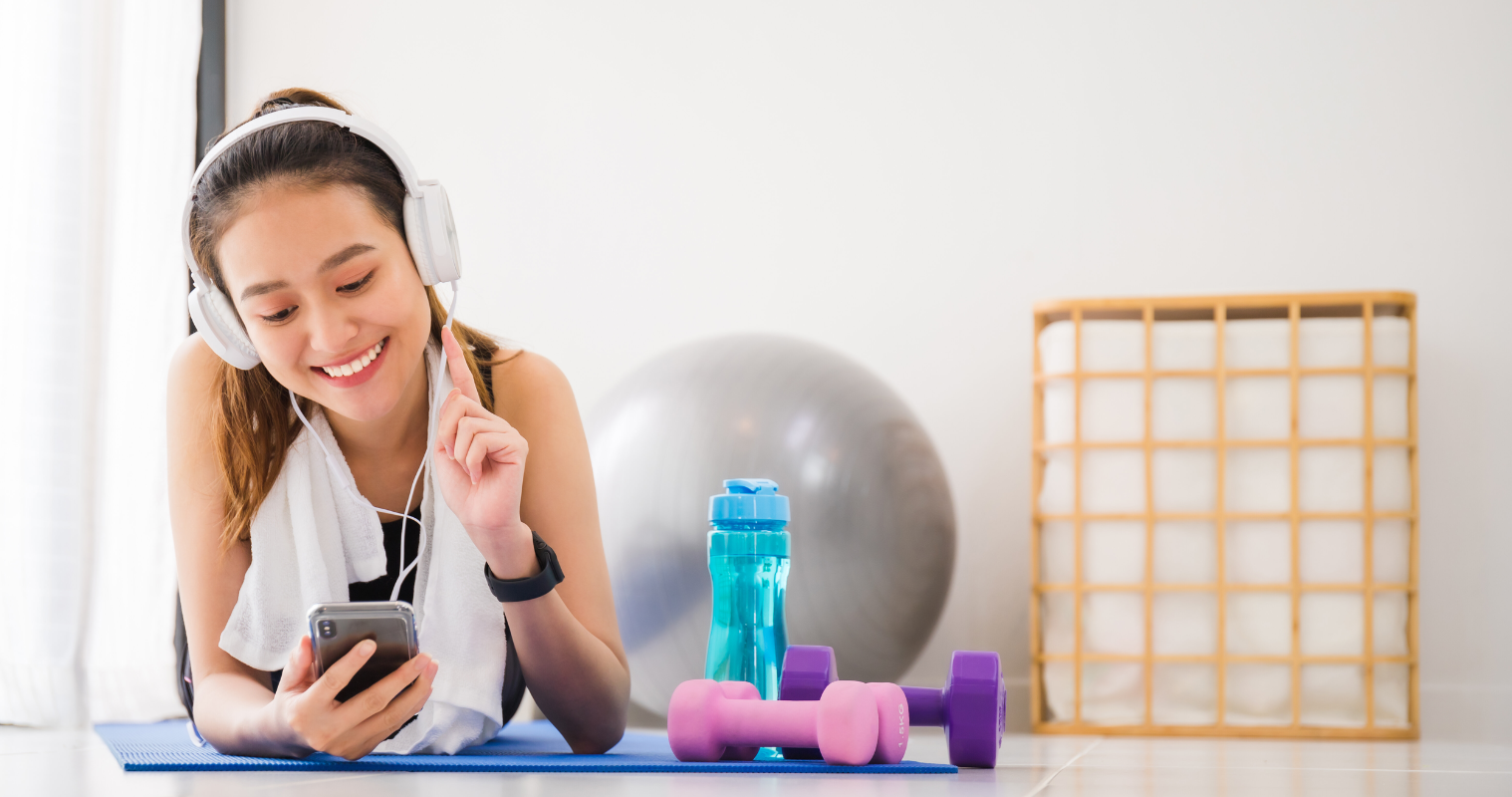 Woman listening to music with headphones and smartphone lying on yoga mat in home gym