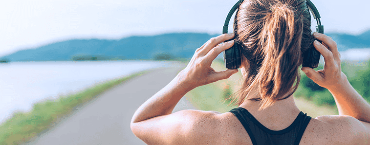 Happy female runner wears earphones while jogging in the morning in nature