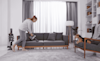 Woman vacuuming her couch with her Pet LG Stick Vacuum with dog watching on an arm chair 