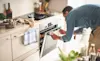 Man in a denim shirt bends to open the under bench oven door to check on dinner